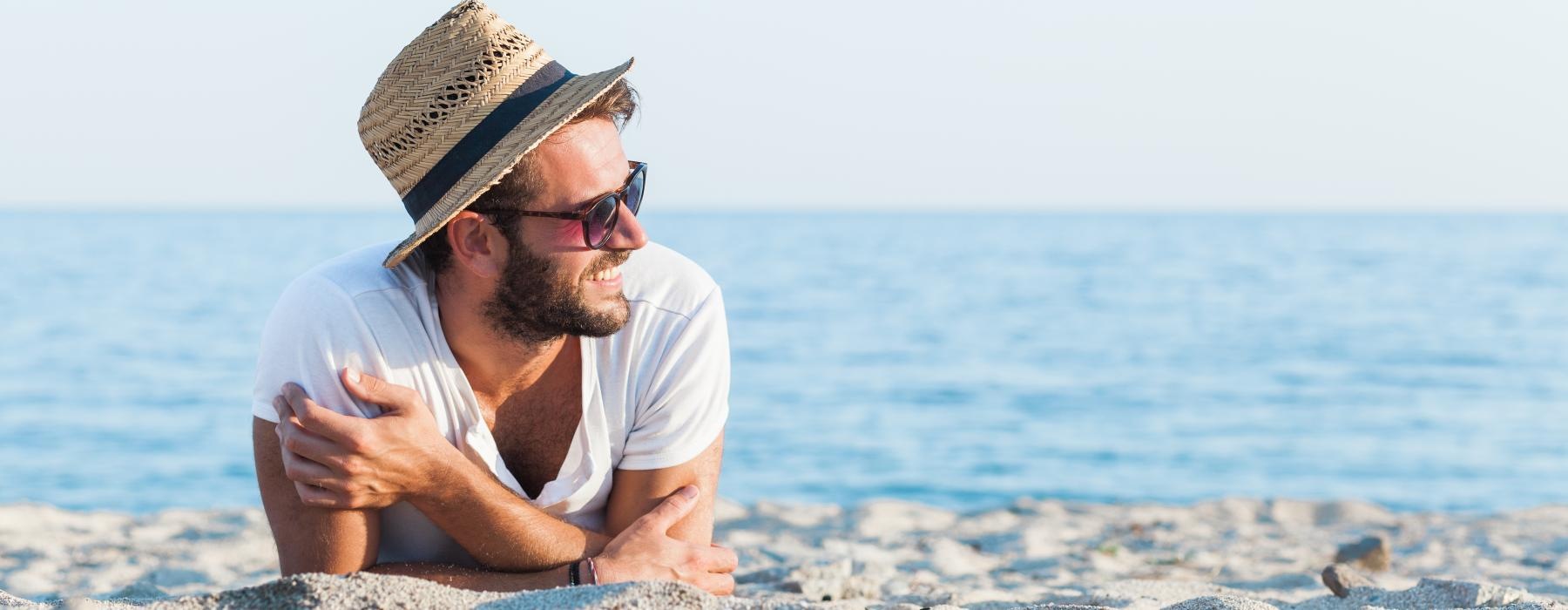a man wearing a hat and sunglasses sitting on a beach